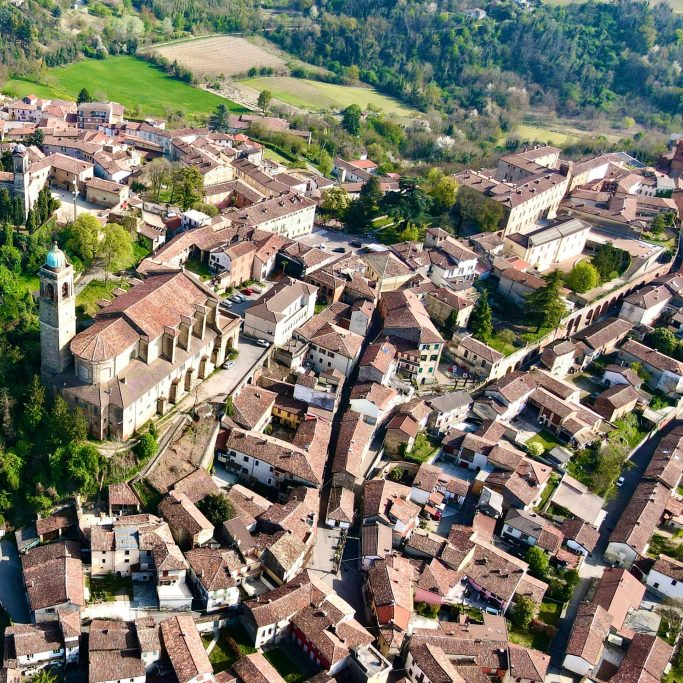 Luftaufnahme der Altstadt von Gavi mit Kirche und umliegender Hügellandschaft.